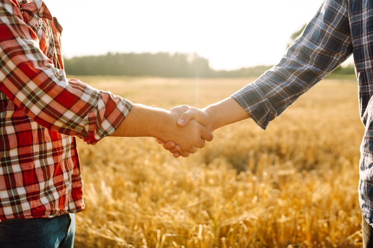 Two people shaking hands in a golden wheat field at sunset, a sign of a genuine partnership